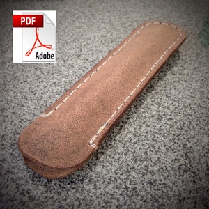 May include: A brown leather pen case with white stitching. The case is made of a soft, textured leather and has a simple, elegant design.
