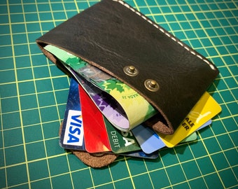 May include: A brown leather wallet with a stitched edge, holding multiple credit cards. The cards are visible and include a VISA card, a DEBIT card, and a card with the text "MADA 20".
