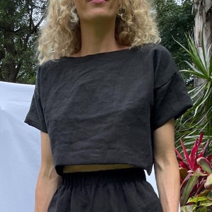 May include: Black linen crop top and matching shorts. The top has a boat neck and short sleeves. The shorts have an elastic waistband. The outfit is made of a lightweight, textured fabric, perfect for warm weather.