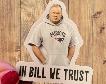 May include: A white sticker featuring a photograph of a man wearing a grey hoodie with the word "Patriots" on it. The sticker also has the text "In Bill We Trust" printed on it.