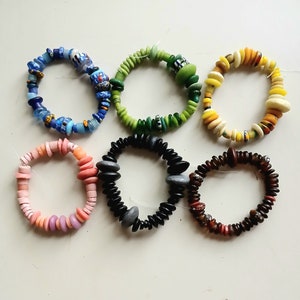 May include: Six colourful beaded bracelets, each with a different pattern and colour scheme. The bracelets are made of glass beads and are arranged in a row on a white surface.