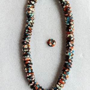 May include: A strand of colorful, patterned beads in shades of orange, blue, and white. The beads are strung together, forming a necklace. A single matching bead is also present. The beads are likely used for jewelry making.