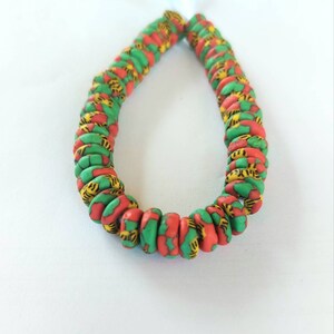 May include: A strand of colorful beads, with a green, red, and yellow pattern. The beads are round and have a slightly textured surface.