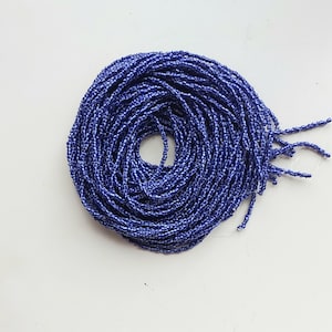 Può includere: Primo piano di una bobina di perline blu scuro. Le perline sono piccole e di dimensioni uniformi, creando una texture liscia e continua.