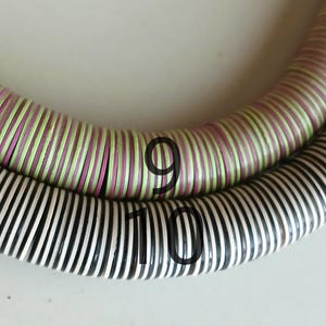 May include: Two strands of colorful, striped, round beads. The top strand is light green and pink, and the bottom strand is black and white. The top strand has the number "9" written on it, and the bottom strand has the number "10" written on it.