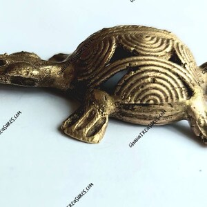 May include: A small, gold-colored turtle figurine with a detailed, patterned shell. The turtle is made of brass and has a smooth, polished finish.