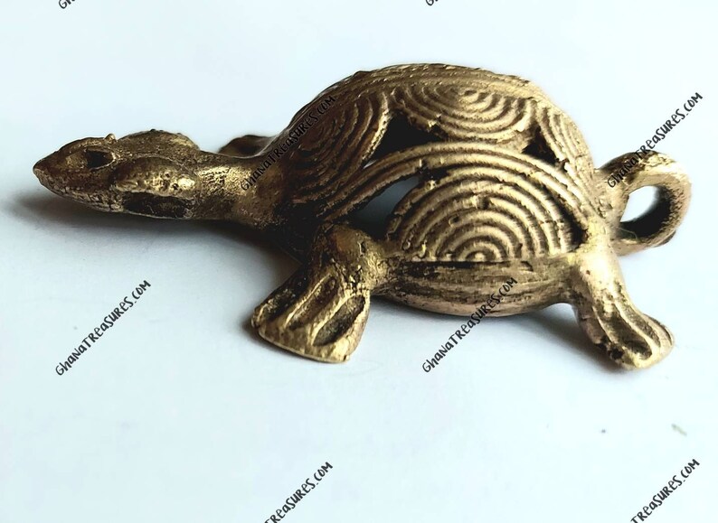 May include: A small, gold-colored turtle figurine with a detailed, patterned shell. The turtle is made of brass and has a smooth, polished finish.