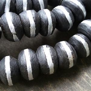 May include: A strand of black wooden beads with white painted stripes. The beads are round and have a smooth, polished finish.