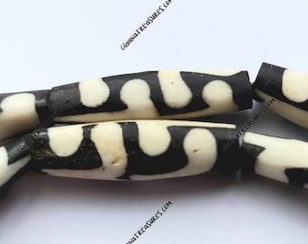 May include: Close-up of black and white cylindrical beads with a geometric pattern. The beads are made of bone or ivory and have a smooth, polished finish.