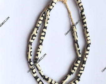 May include: A necklace made of black and white cylindrical beads with a geometric pattern. The beads are strung on a natural fiber cord.