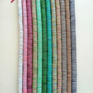 May include: A set of 14 colorful wooden bead strands, each strand is made of stacked round wooden beads with a different color pattern. The beads are stacked on a string and tied at the top with a pink string.