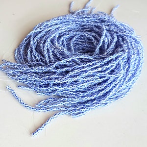 Könnte beinhalten: Ein aufgerolltes Bündel aus mehreren Strängen kleiner, zylindrischer Saatperlen. Jede einzelne Perle weist ein ausgeprägtes Muster aus abwechselnden horizontalen Streifen in leuchtendem Blau und Weiß auf, aufgereiht auf dünnem, klarem Monofilamentfaden.