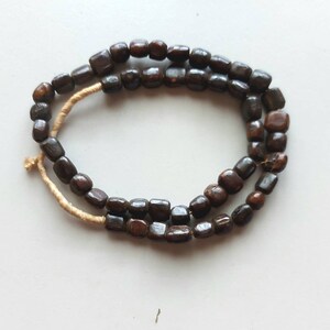 May include: A strand of dark brown wooden beads, strung together with a thin, beige cord.