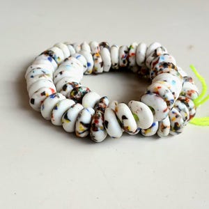 May include: A bracelet made of white, oval-shaped beads with colorful speckles of blue, red, yellow, and black. The beads are strung together, forming a circular shape. Bright green string is attached.