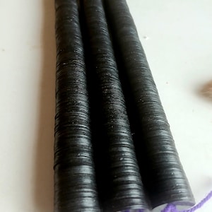 May include: Three black, cylindrical objects with a textured surface, possibly beads or decorative elements. Each has a purple string attached at one end. The objects are arranged parallel to each other against a white background.