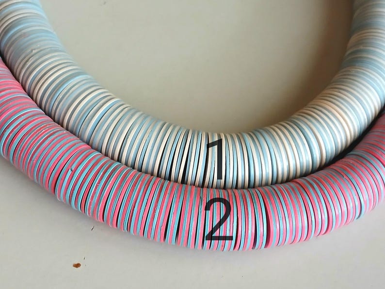 May include: Two strands of colorful round beads, one strand is white and blue, the other is pink and blue. The strands are labeled with the numbers 1 and 2.