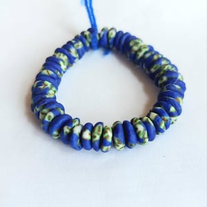 May include: A blue and white beaded bracelet with a green and white pattern. The bracelet is made of small, round beads that are strung together on a blue cord.