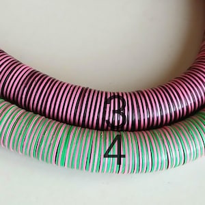 May include: Two strands of colorful, round beads, one pink and black, the other green and pink. The beads are stacked on top of each other, forming a circle.