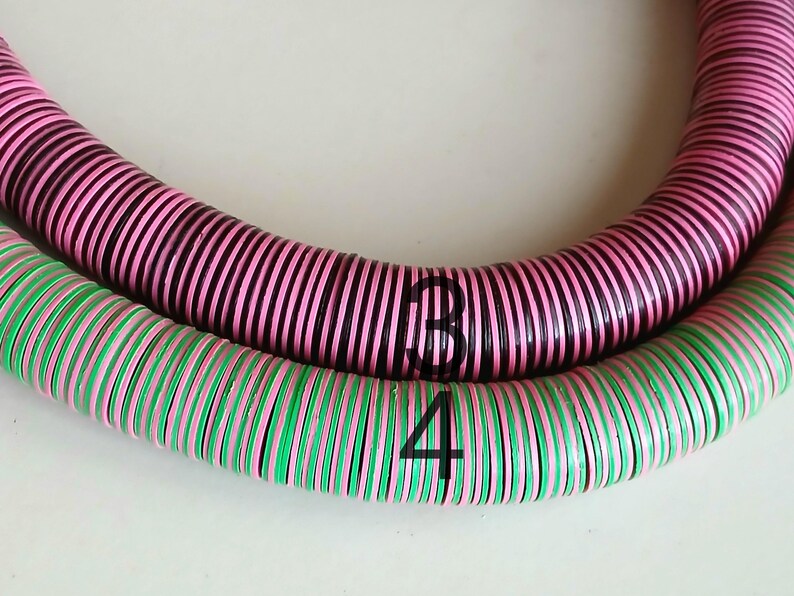 May include: Two strands of colorful, round beads, one pink and black, the other green and pink. The beads are stacked on top of each other, forming a circle.
