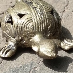 May include: A small, gold-colored turtle figurine with intricate details on its shell. The turtle is lying on its belly with its head turned to the side.