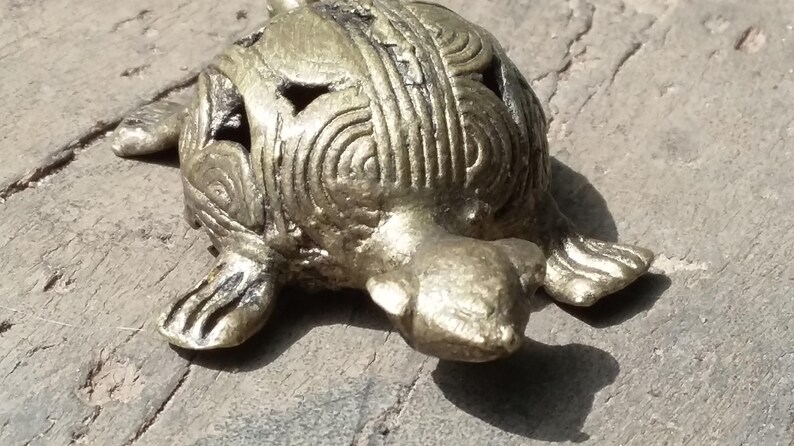 May include: A small, gold-colored turtle figurine with intricate details on its shell. The turtle is lying on its belly with its head turned to the side.