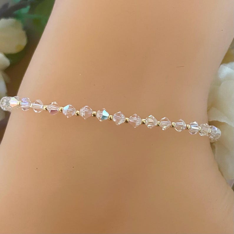 May include: A delicate bracelet featuring iridescent crystal beads strung on a gold-colored chain. The crystals reflect light, creating a shimmering effect. This jewelry piece is a subtle and elegant accessory.