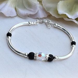 May include: A silver bracelet with black lava beads and a clear crystal charm.
