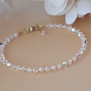 May include: Delicate bracelet featuring clear, faceted crystal beads interspersed with small gold-colored beads. The bracelet has a gold-colored clasp and is displayed on a neutral background, suggesting a jewelry or accessory theme.