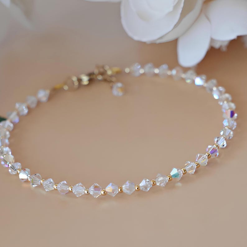 May include: Delicate bracelet featuring clear, faceted crystal beads interspersed with small gold-colored beads. The bracelet has a gold-colored clasp and is displayed on a neutral background, suggesting a jewelry or accessory theme.