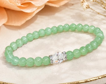May include: A stretch bracelet composed of smooth, round, light green beads. The bracelet features a single, central, clear faceted crystal bead flanked by two small silver-toned metal spacers embedded with tiny clear stones.