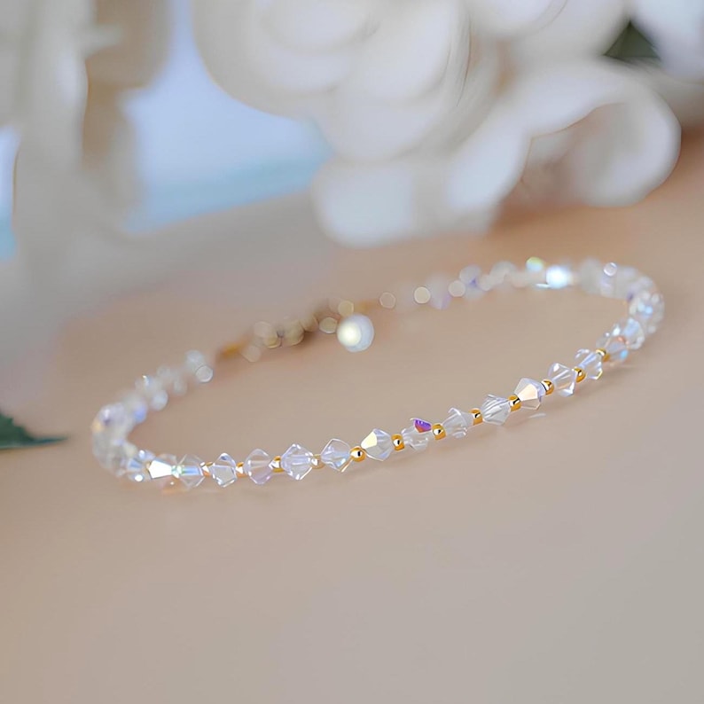 May include: A delicate bracelet featuring clear, faceted crystal beads interspersed with small gold-colored beads. The bracelet has a delicate clasp and is designed to be worn around the wrist. The crystals catch the light, creating a sparkling effect.
