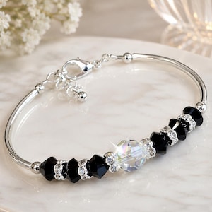 May include: A silver bracelet with black and clear crystal beads. The bracelet has a delicate design with a clasp closure. The beads are faceted and sparkle, adding a touch of elegance to the jewelry.