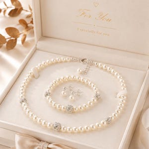 May include: A jewellery set consisting of a pearl necklace, a pearl bracelet, and a pair of pearl earrings. The necklace and bracelet feature white pearls interspersed with round, silver-toned crystal-encrusted beads. The set is in a box.