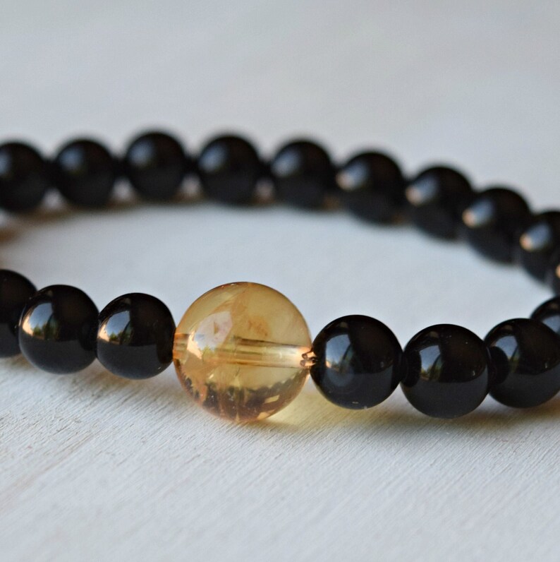 May include: A black beaded bracelet with a single amber bead in the center.