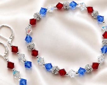 May include: A jewelry set featuring a bracelet and matching earrings. The set includes red, white, and blue crystal beads, interspersed with silver-colored metal beads. The earrings have a lever back closure. The bracelet and earrings are displayed on a white satin surface.