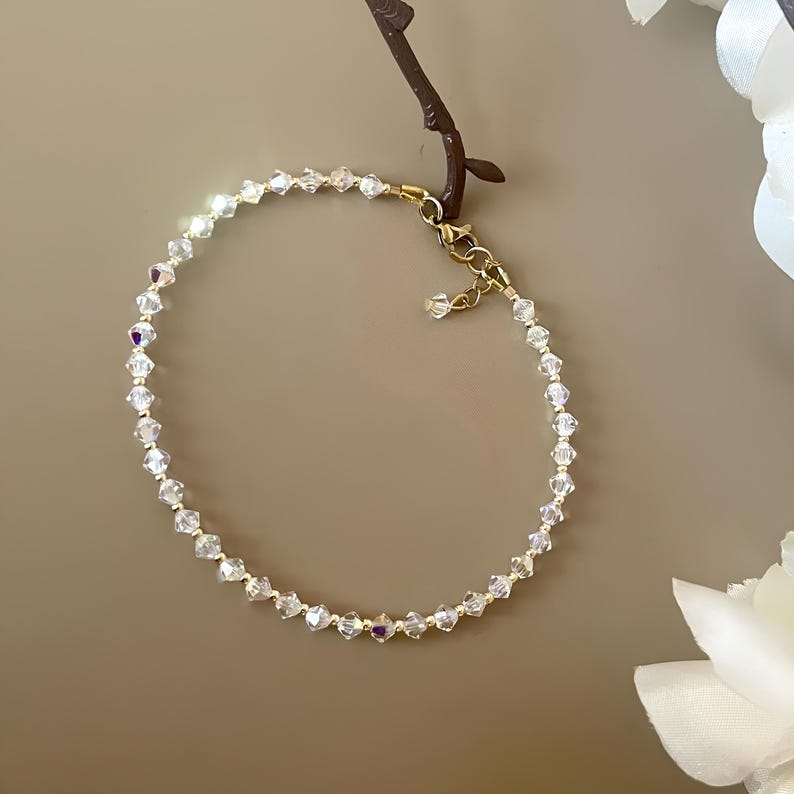 May include: A delicate bracelet featuring clear, faceted crystal beads strung on a gold-toned chain. The bracelet has a lobster clasp closure and an adjustable length. The crystals sparkle, reflecting light. This elegant piece is suitable for special occasions.