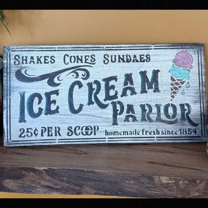 May include: Wooden sign for an ice cream parlor, featuring the words "Ice Cream Parlor" in a vintage font. The sign includes illustrations of an ice cream cone and the text "25¢ per scoop, homemade fresh since 1854."