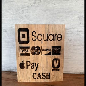 May include: Wooden sign with the Square logo and payment options including Visa, Mastercard, Discover, American Express, Apple Pay, Venmo, and the word CASH. The sign is made of light-colored wood.