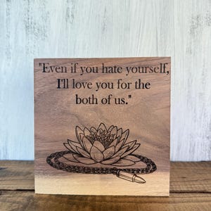 May include: A wooden block with engraved text: "Even if you hate yourself, I'll love you for the both of us." Below the text is an engraved lotus flower with a chain and a bullet.