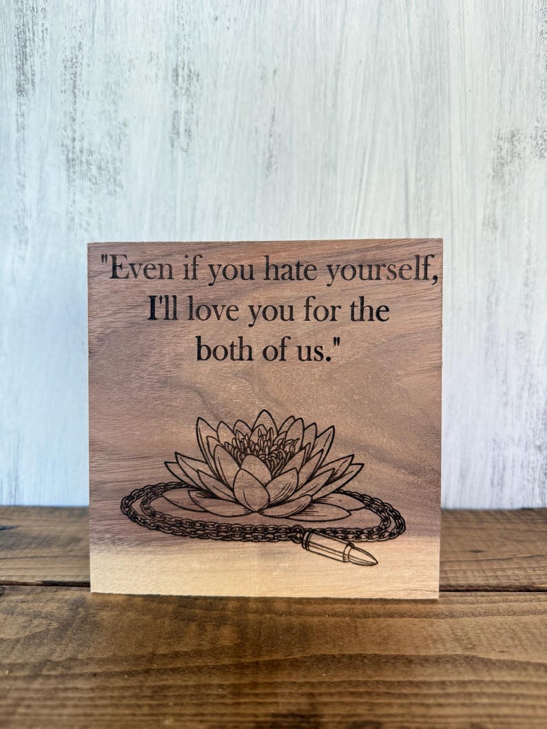 May include: A wooden block with engraved text: "Even if you hate yourself, I'll love you for the both of us." Below the text is an engraved lotus flower with a chain and a bullet.