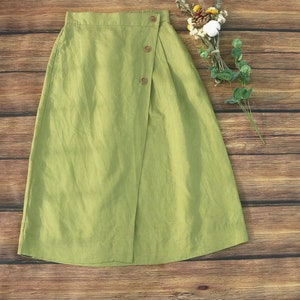 May include: A green linen skirt with a wrap-around design and button closures. The skirt has a relaxed fit and a midi length.