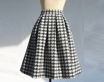 May include: A black and white houndstooth patterned skirt with pleats. The skirt is knee-length and has a fitted waist.