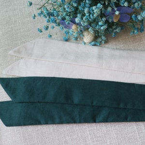 May include: Two fabric ribbon ties, one is a dark green color and the other is a light beige color. The ties are folded and stacked on top of each other.