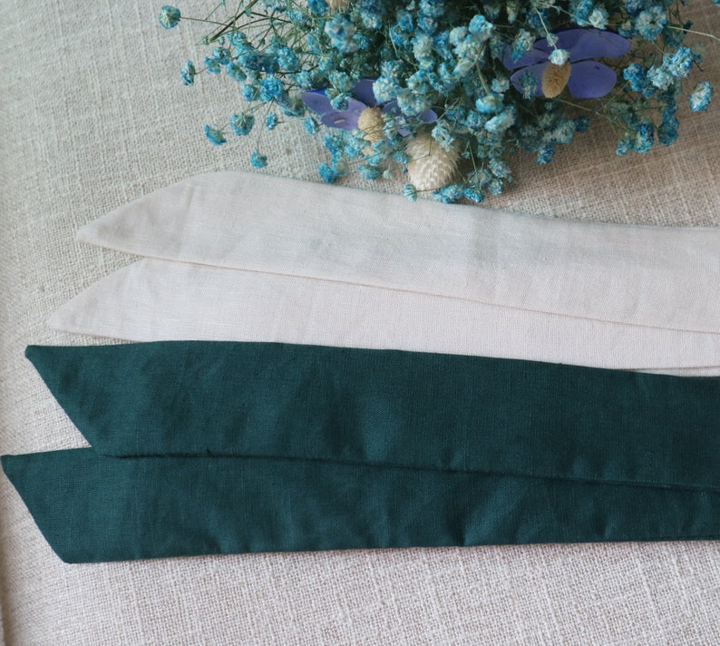 May include: Two fabric ribbon ties, one is a dark green color and the other is a light beige color. The ties are folded and stacked on top of each other.