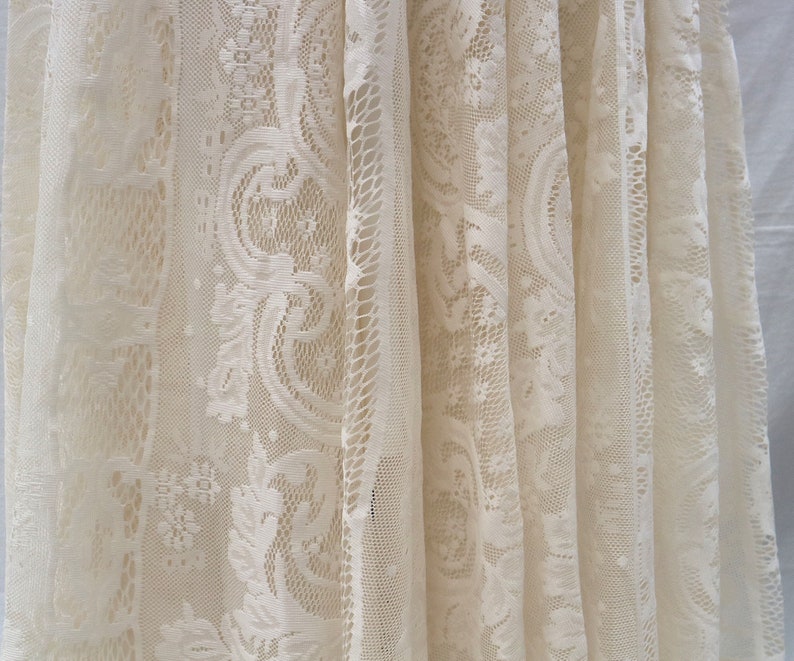 May include: White lace fabric with a delicate floral pattern. The fabric is sheer and has a soft, flowing texture.