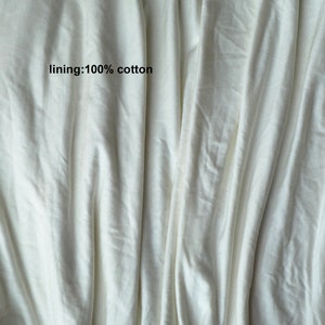 May include: Close-up of a white fabric with a smooth texture. The fabric is folded and has a slight sheen. The text "lining: 100% cotton" is printed on the fabric.