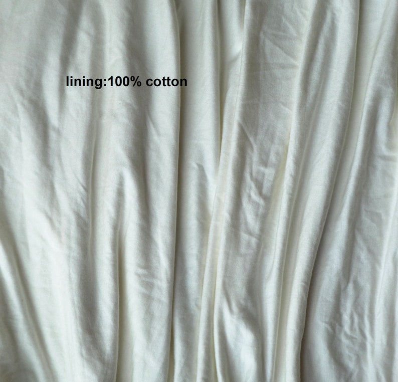 May include: Close-up of a white fabric with a smooth texture. The fabric is folded and has a slight sheen. The text "lining: 100% cotton" is printed on the fabric.