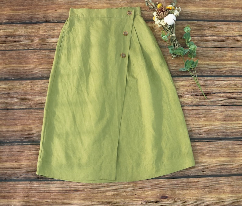 May include: A green linen skirt with a wrap-around design and button closures. The skirt has a relaxed fit and a midi length.