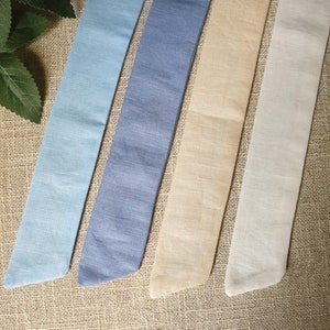 May include: Four fabric ribbon strips in different shades of blue, beige, and white. The ribbons are arranged horizontally on a brown burlap background.