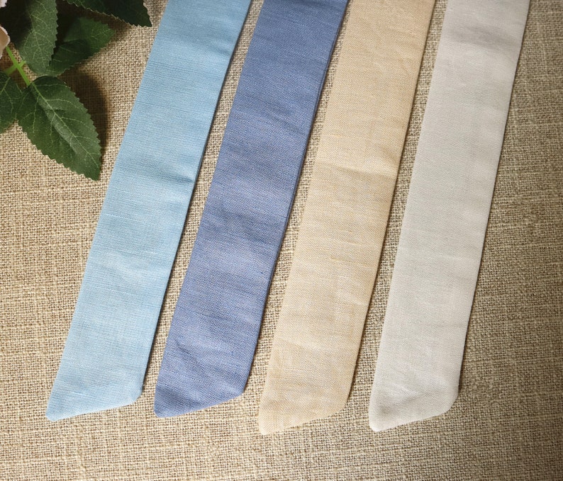 May include: Four fabric ribbon strips in different shades of blue, beige, and white. The ribbons are arranged horizontally on a brown burlap background.